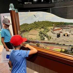 Two children wearing hats are looking at a museum exhibit featuring trains.